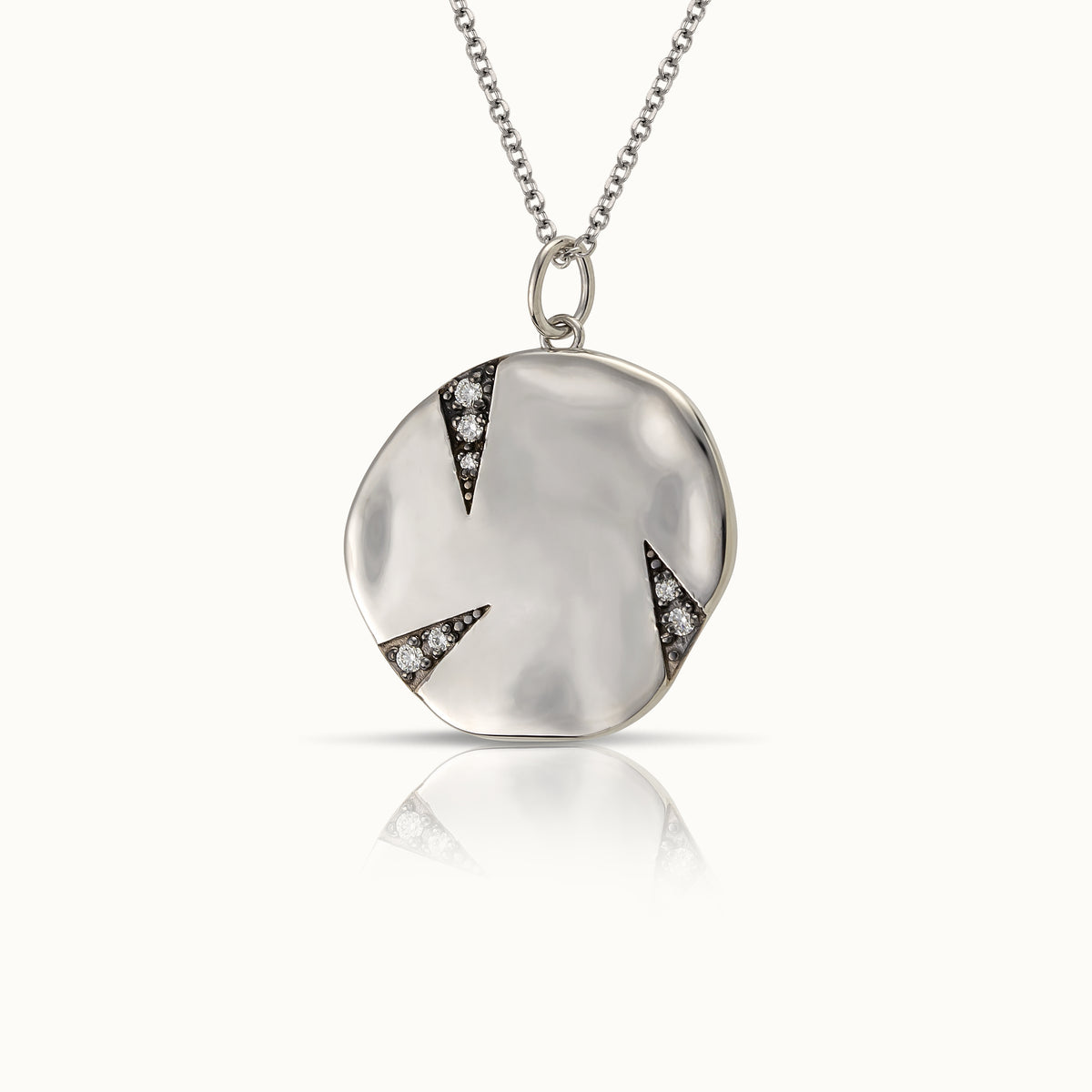 925 sterling silver necklace featuring a polished, slightly irregular round pendant with three dark triangular insets set with small clear faceted stones, suspended from a fine link chain against a warm off-white background.